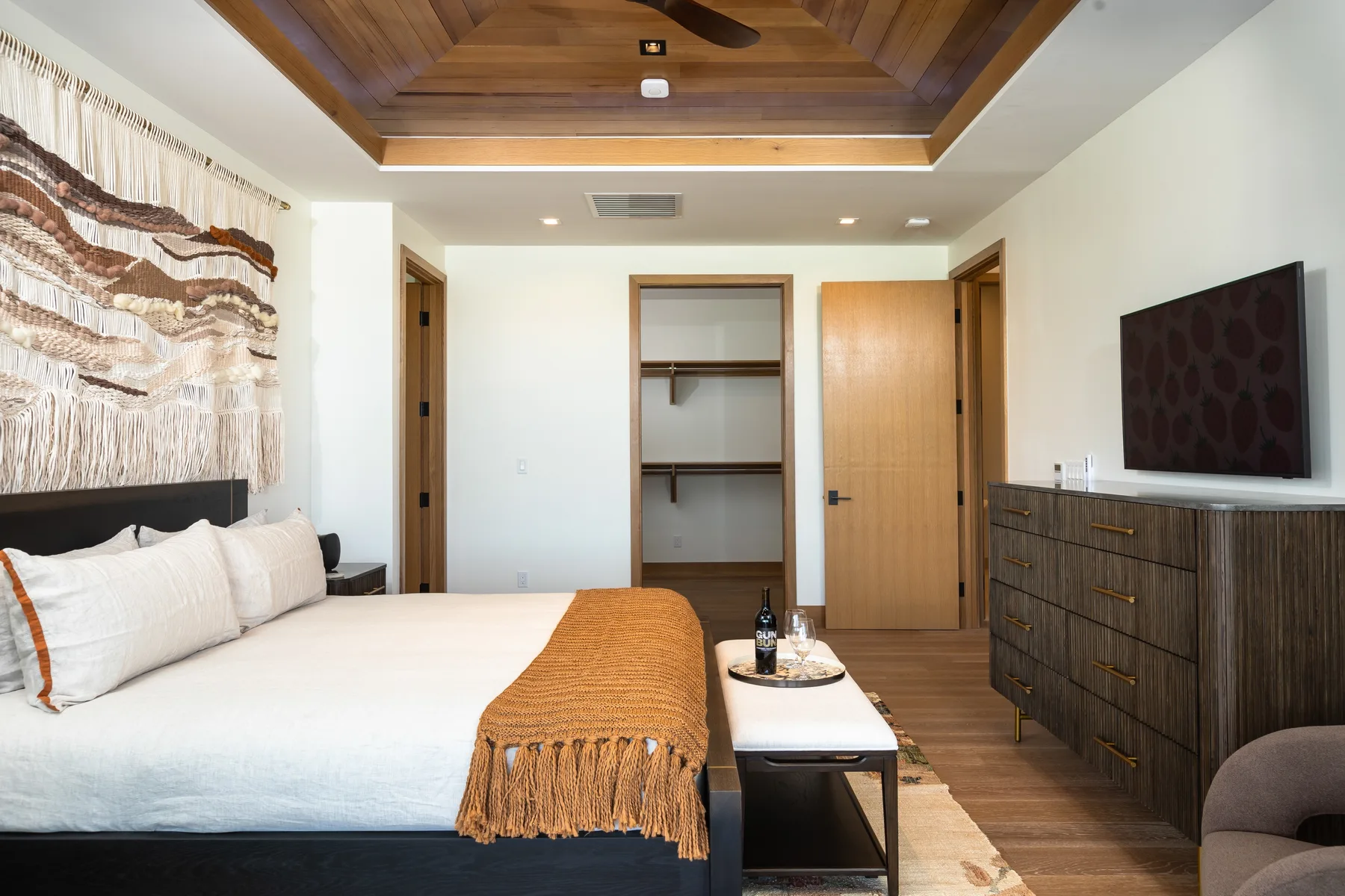A bedroom with a large bed, a wooden ceiling, and a dresser beneath a wall-mounted television.