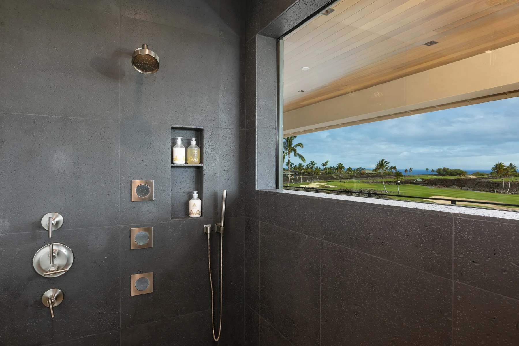 A dark-tiled shower area opens onto a wide window with a tropical landscape view.