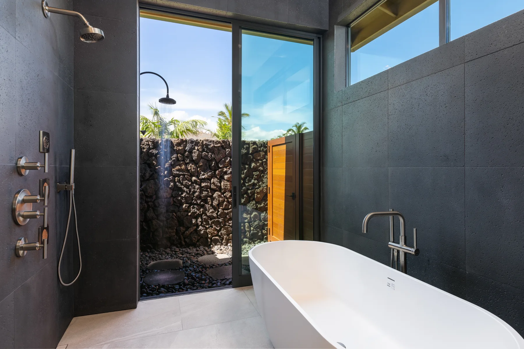 A bathroom with a freestanding bathtub beside a glass door opening to a walled outdoor area.