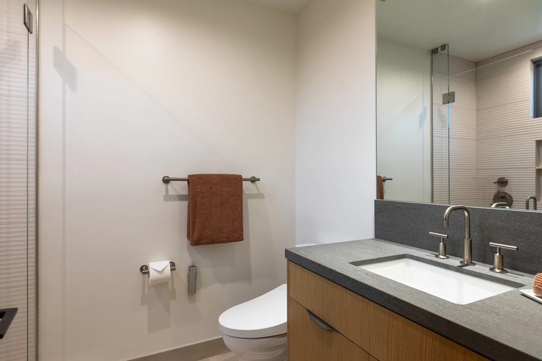 A bathroom with a vanity, sink, and toilet beside a large wall mirror.