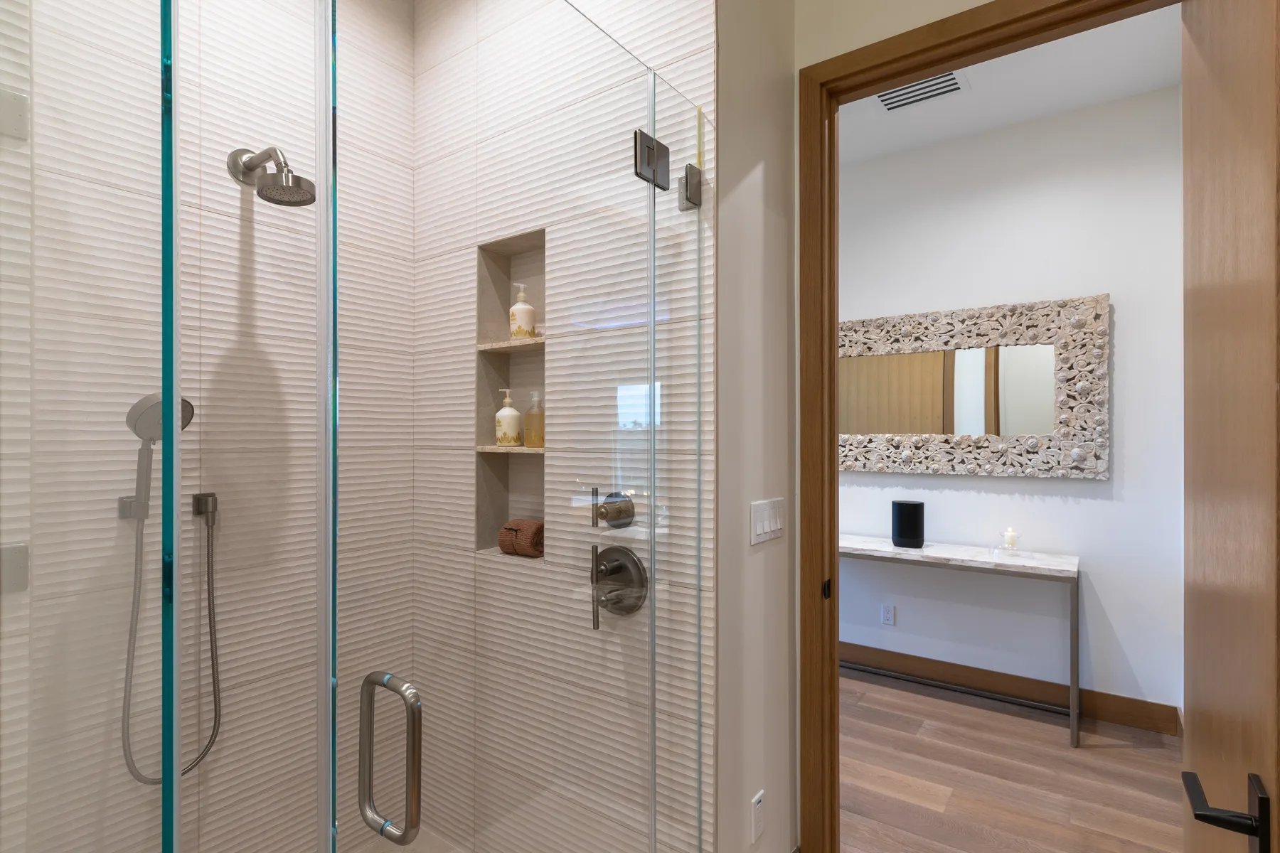 A tiled bathroom with a glass shower beside a vanity and wall mirror.