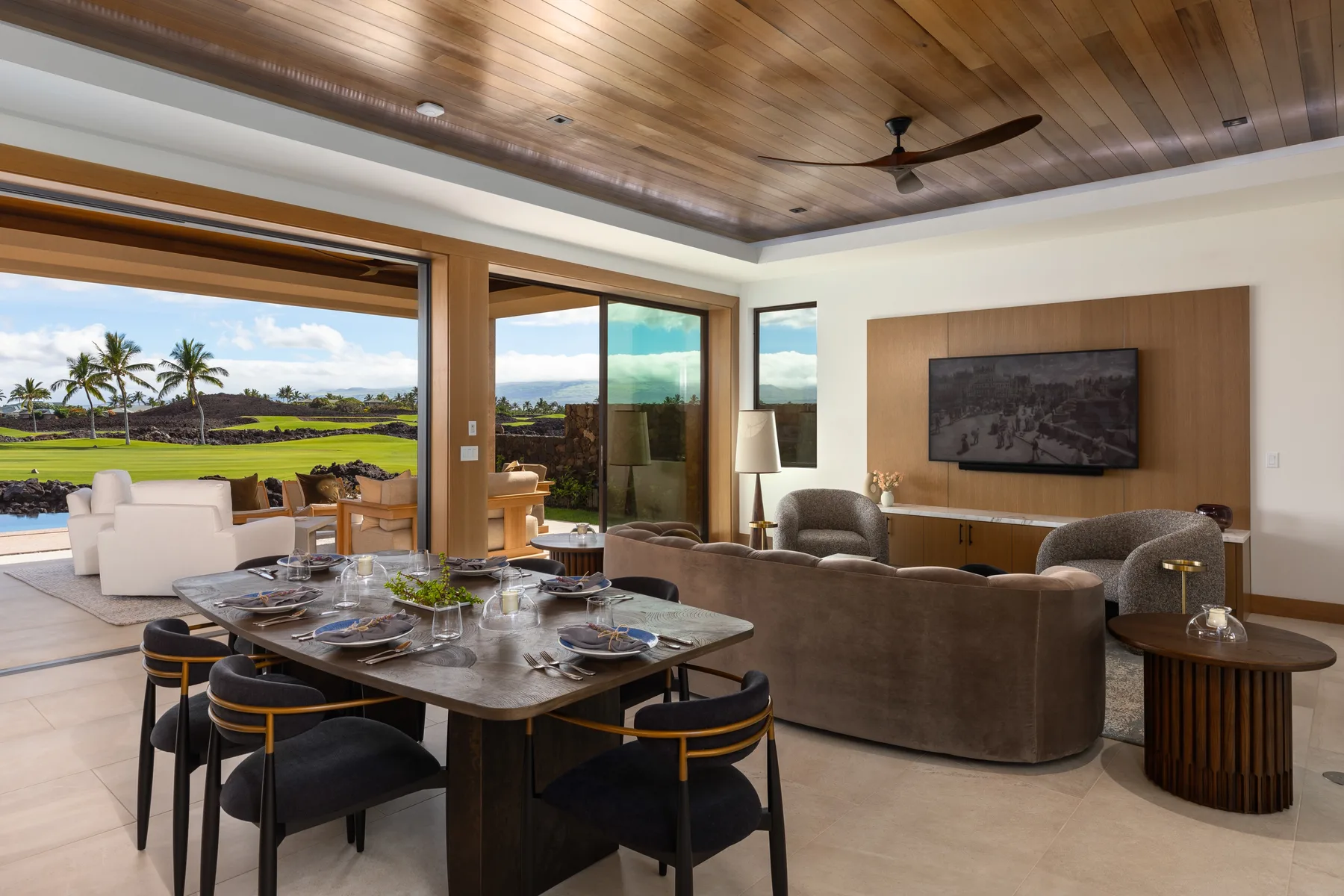 A modern living and dining area opens onto a patio with views of landscaped grounds.