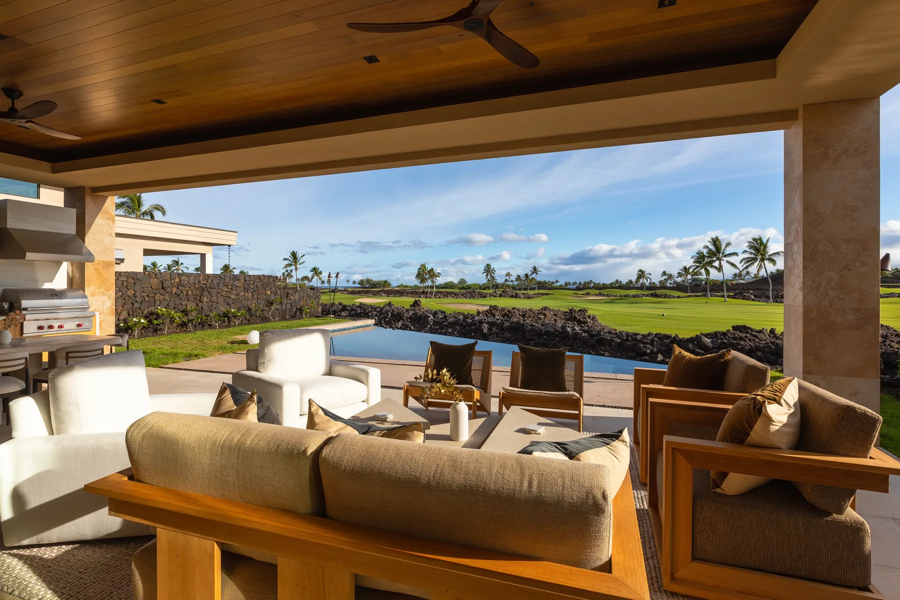 A covered outdoor lounge overlooks a pool, green lawn, and palm trees.