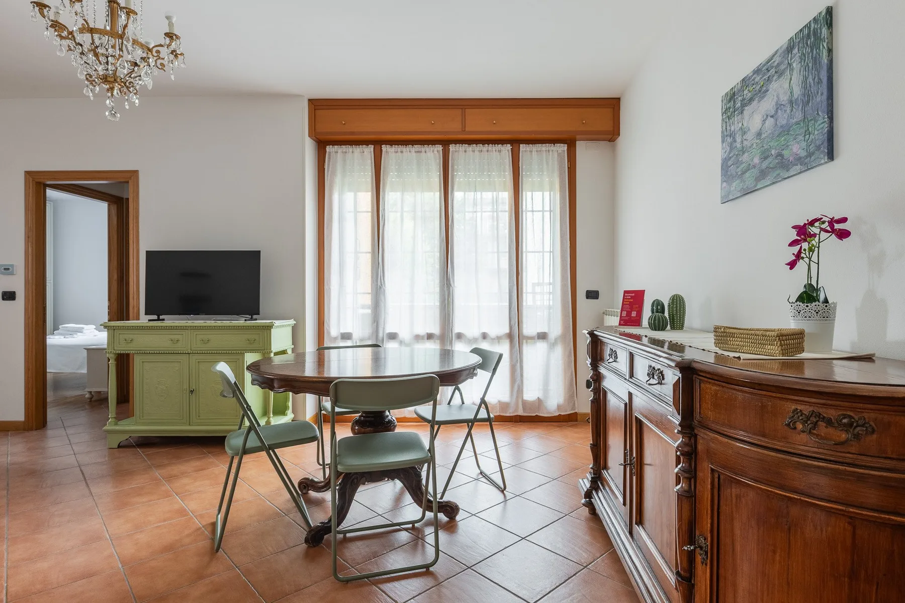 A dining area with a round table and chairs beside tall curtained windows.
