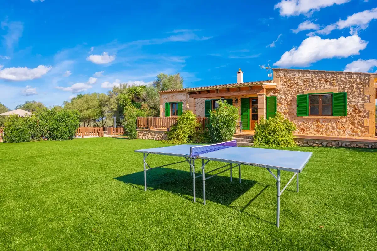 A stone house with green shutters overlooks a lawn with a table tennis table.