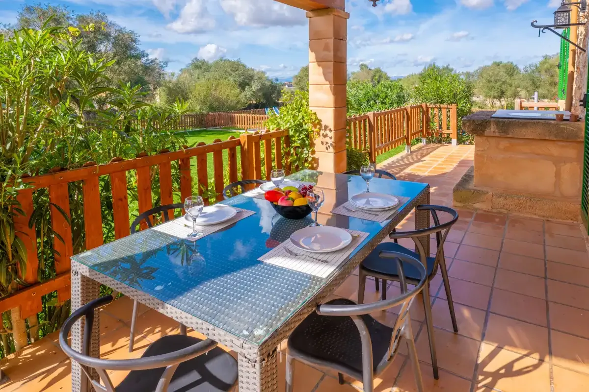 An outdoor dining area with a set table and views of green gardens.