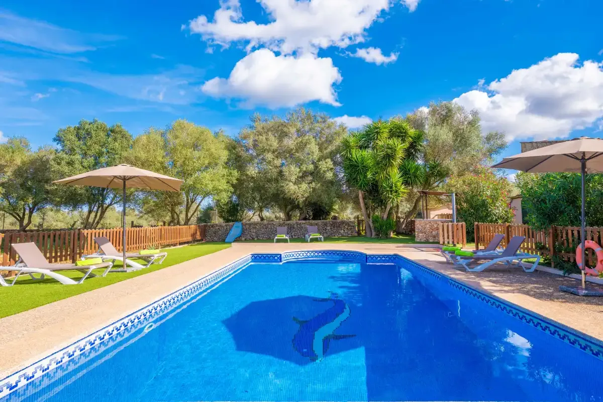 An outdoor swimming pool sits beside a sunny patio with loungers and umbrellas.