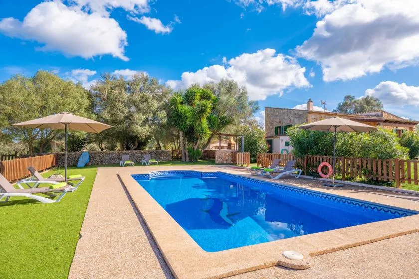 Outdoor swimming pool surrounded by lounge seating, umbrellas, and greenery.