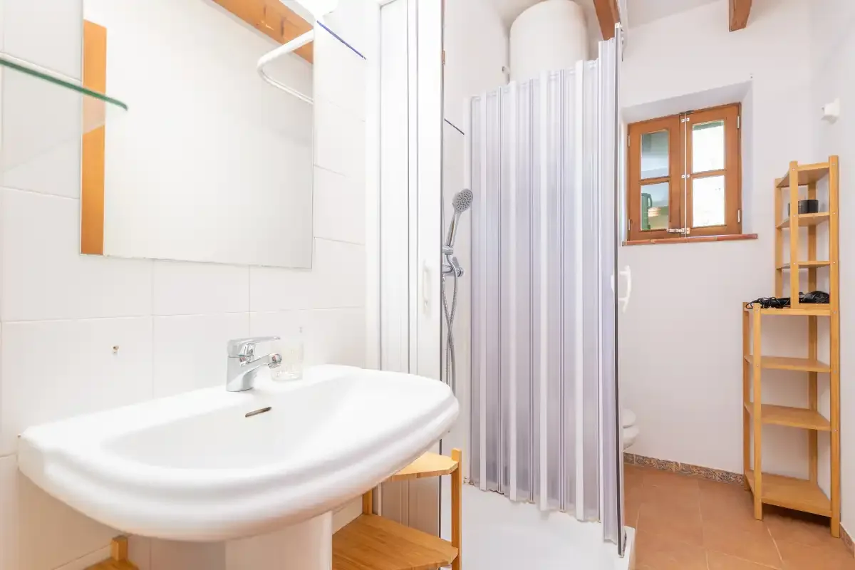 A bright bathroom with a sink, shower, and window.