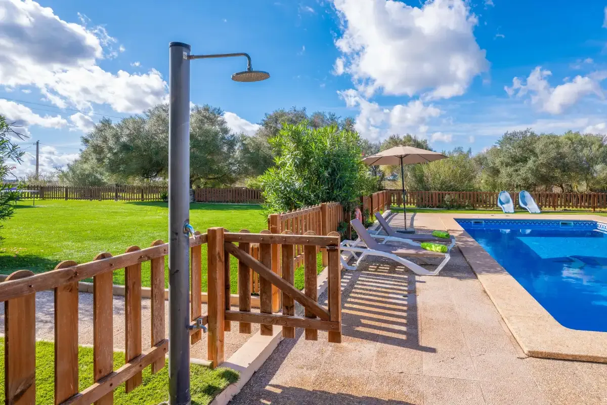 An outdoor swimming pool beside a wooden fence and lounge seating.