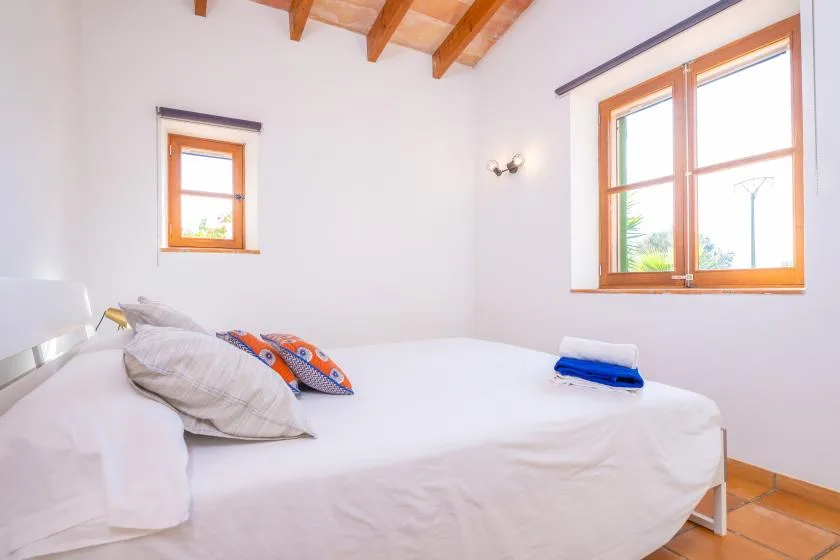 A bright bedroom with a bed beneath two windows.