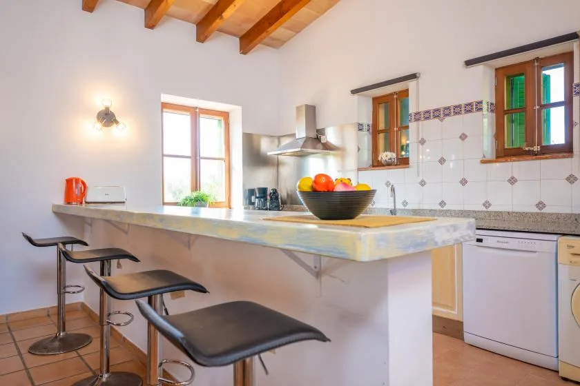 A bright kitchen with a central counter and wooden ceiling beams.