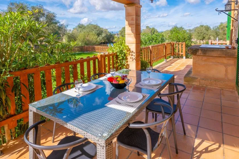 A tiled outdoor dining terrace has a glass table set beside a wooden railing.