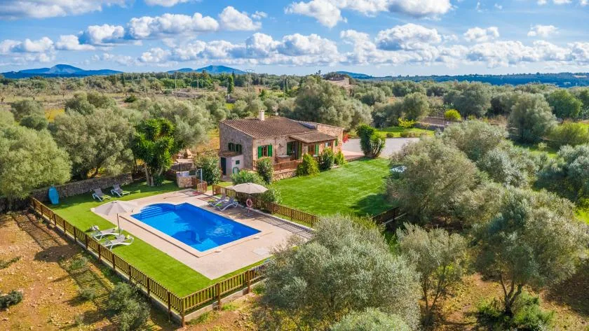 A countryside house sits among trees beside a swimming pool and lawn.