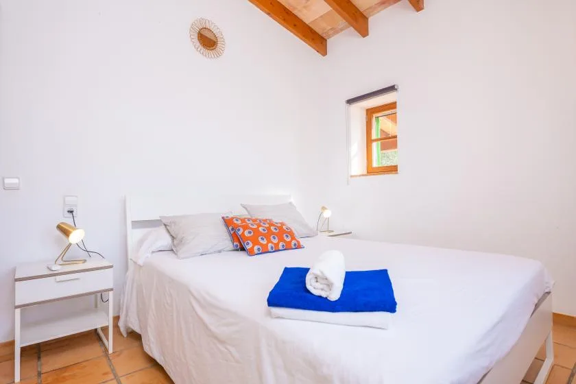 A bright bedroom with a bed dressed in white and a colorful accent pillow.