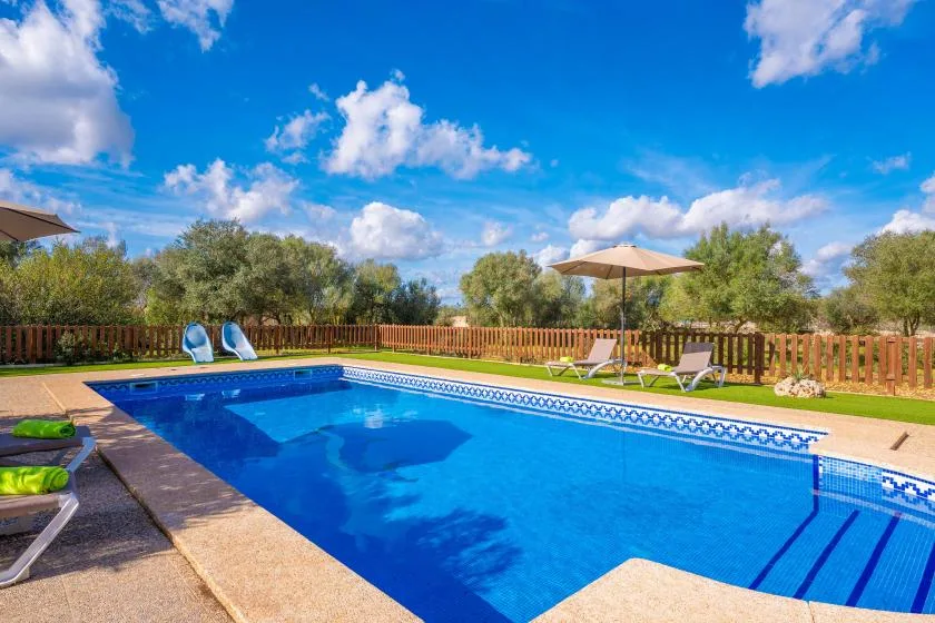 Outdoor swimming pool with lounge chairs and umbrellas beside a wooden fence.