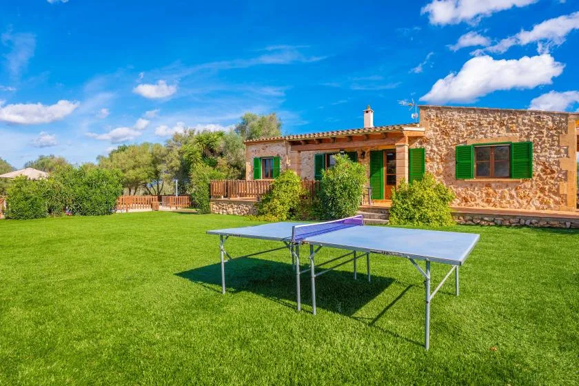 A stone house faces a green lawn with a table tennis table in front.