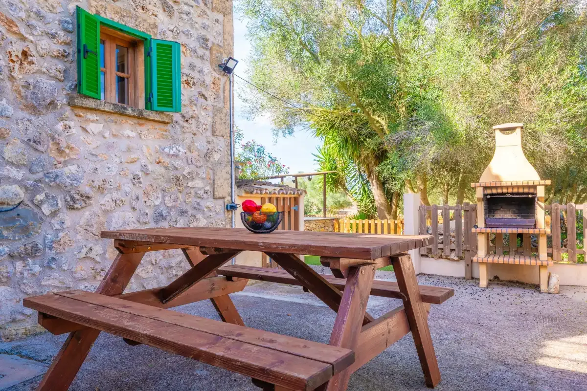 A stone courtyard with a wooden picnic table and an outdoor grill.