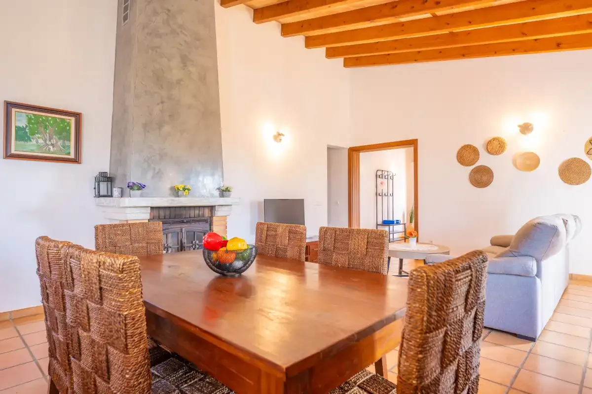 A dining area with a large wooden table and woven seating beside a fireplace.