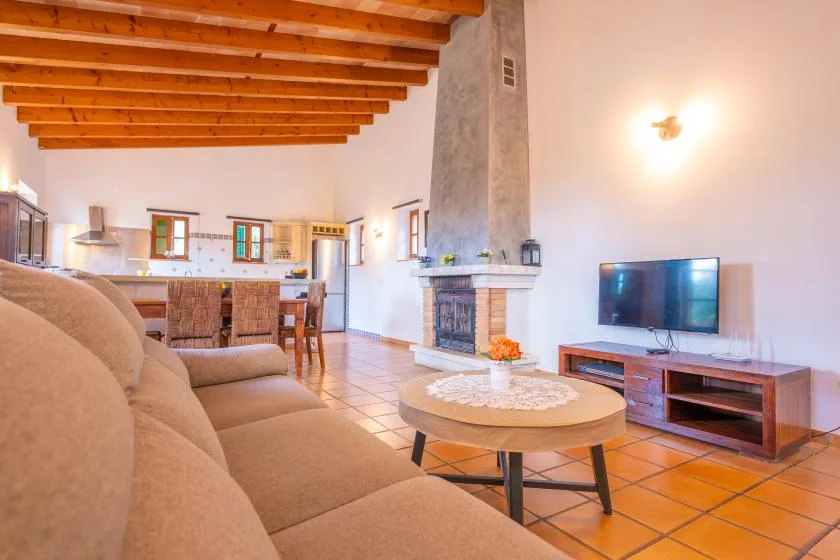A living room opens onto a kitchen, with seating facing a fireplace and television.