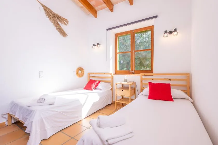 A bedroom with two beds beneath a window and exposed wooden ceiling beams.