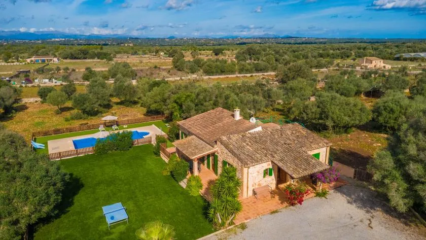 Aerial view of a country house with a tiled roof, lawn, and swimming pool.