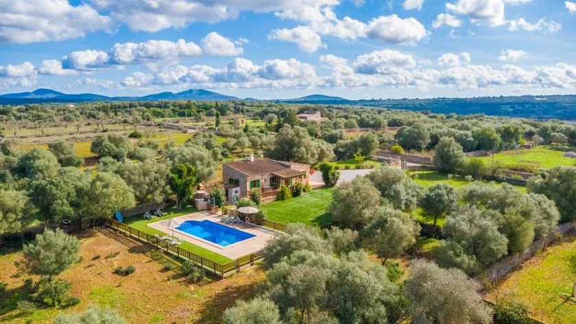 An aerial view shows a countryside house beside a blue swimming pool.