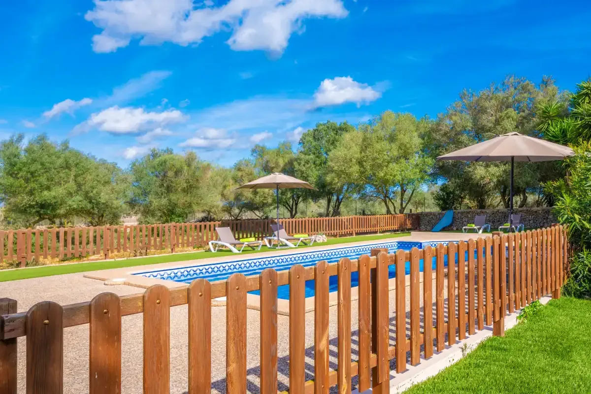 An outdoor swimming pool is surrounded by a wooden fence and green lawn.