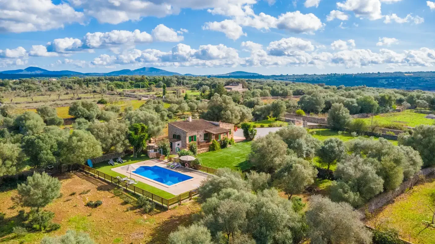 A rural property sits among green fields and trees, with a swimming pool nearby.