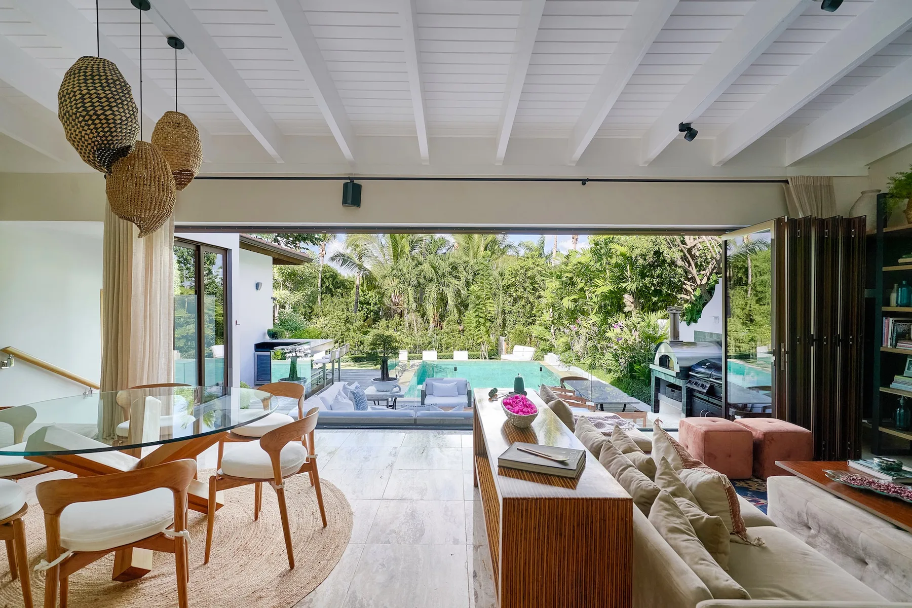 An open living and dining area looks out onto a pool and lush greenery.