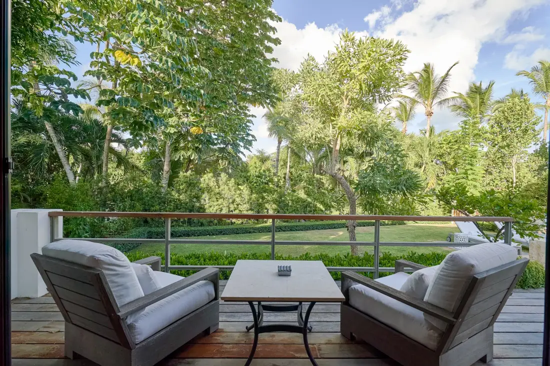 An outdoor seating area overlooks a lush garden, with a low table between two cushioned seats.