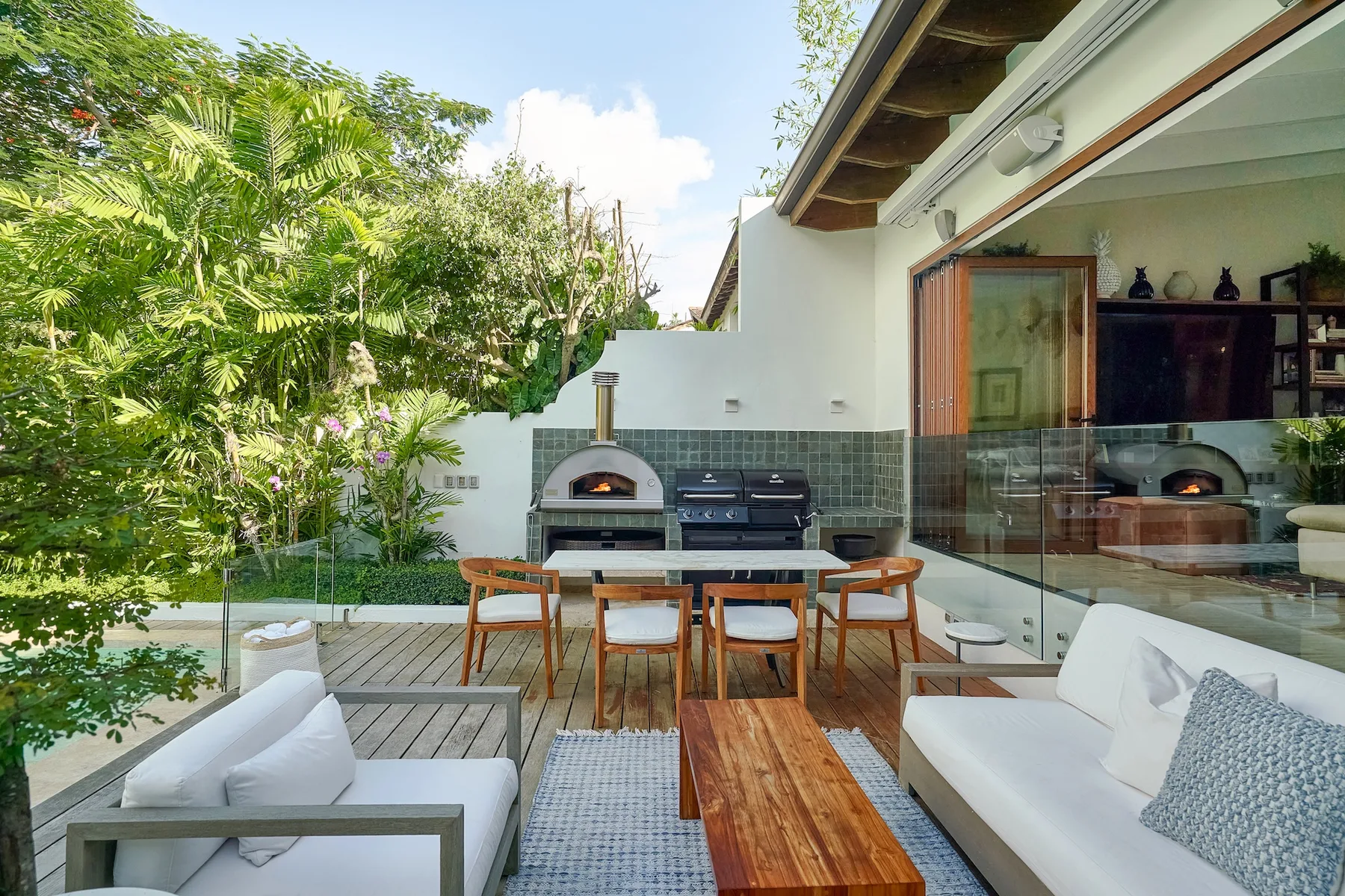 An outdoor dining and lounge area beside a garden, with a built-in grill.
