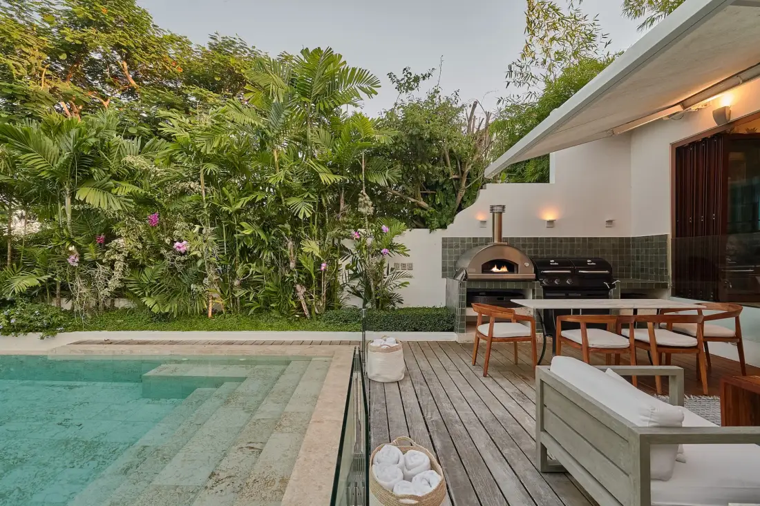 An outdoor pool beside a wooden deck with a dining table and cooking area.