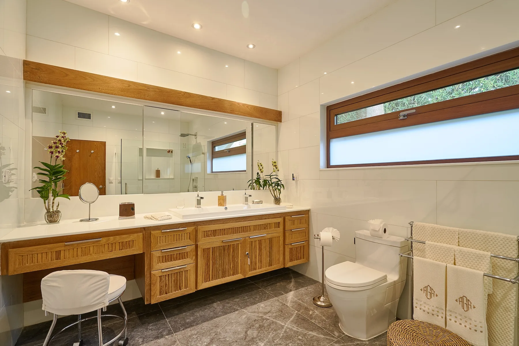 A bright bathroom with a long vanity, large mirror, and window.