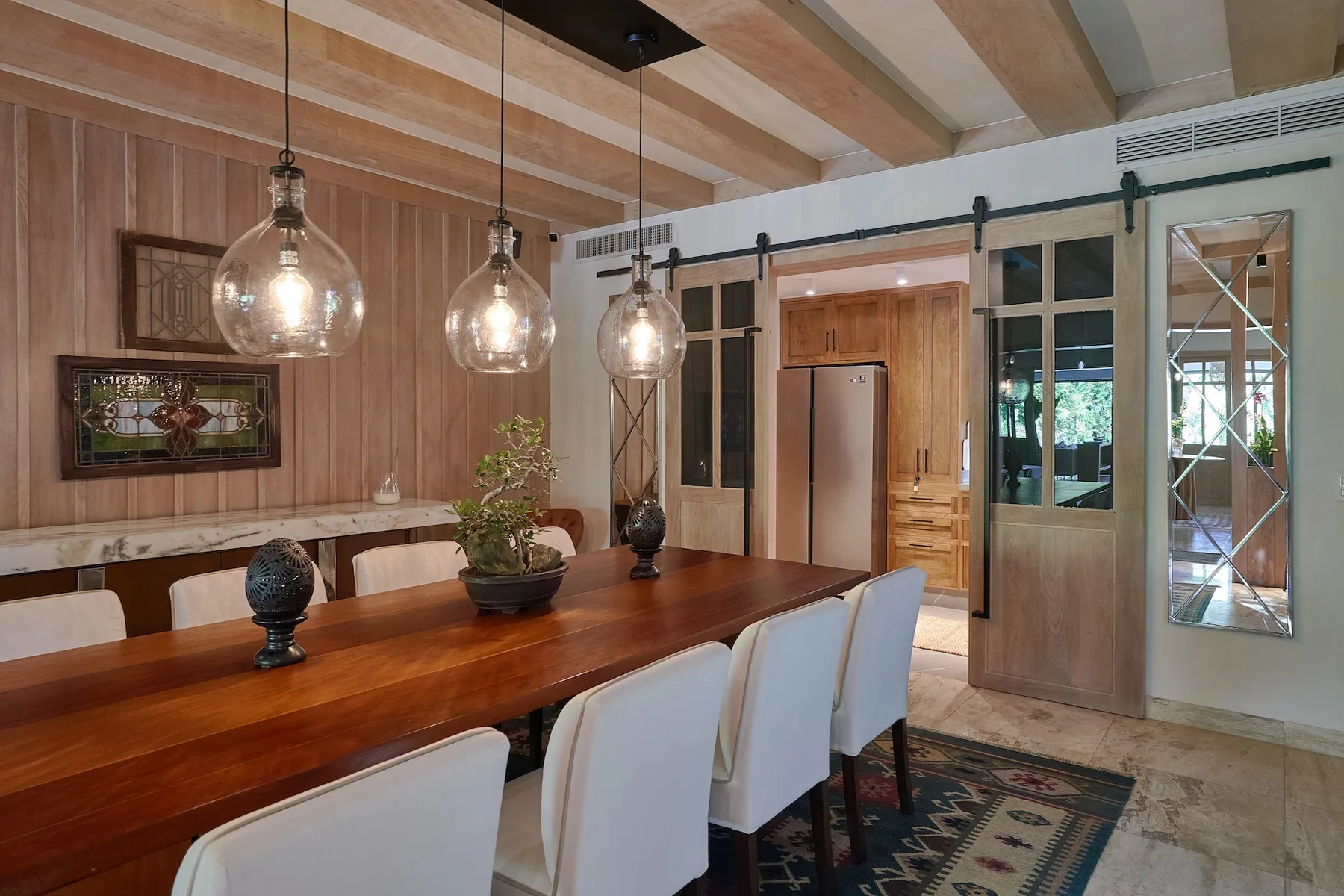 A dining area with a long wooden table, pendant lights, and upholstered seating.