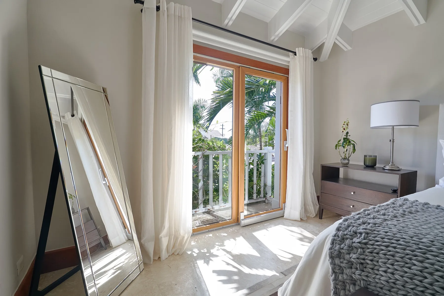 A bright bedroom with a bed beside glass doors opening onto a balcony.