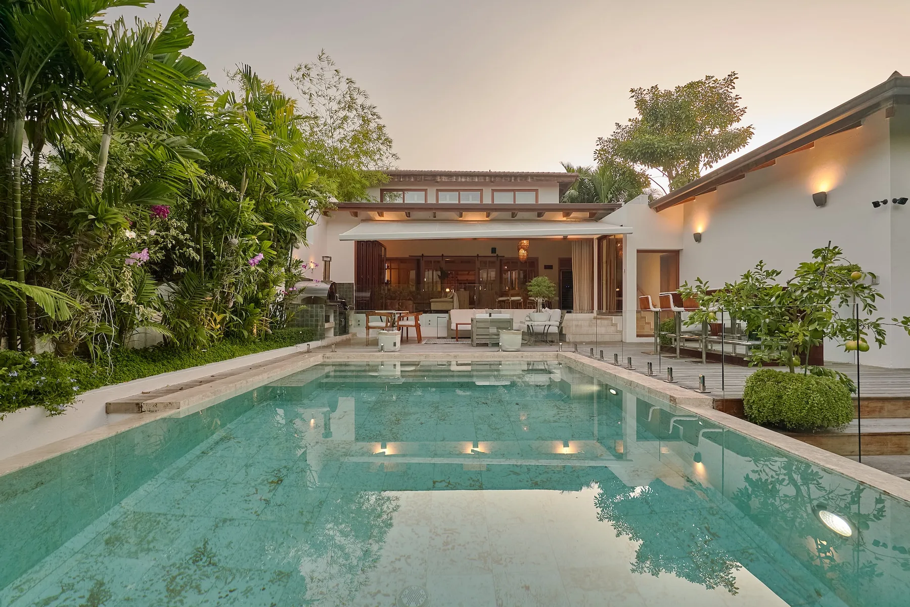 Una piscina frente a una casa moderna, rodeada de plantas tropicales.