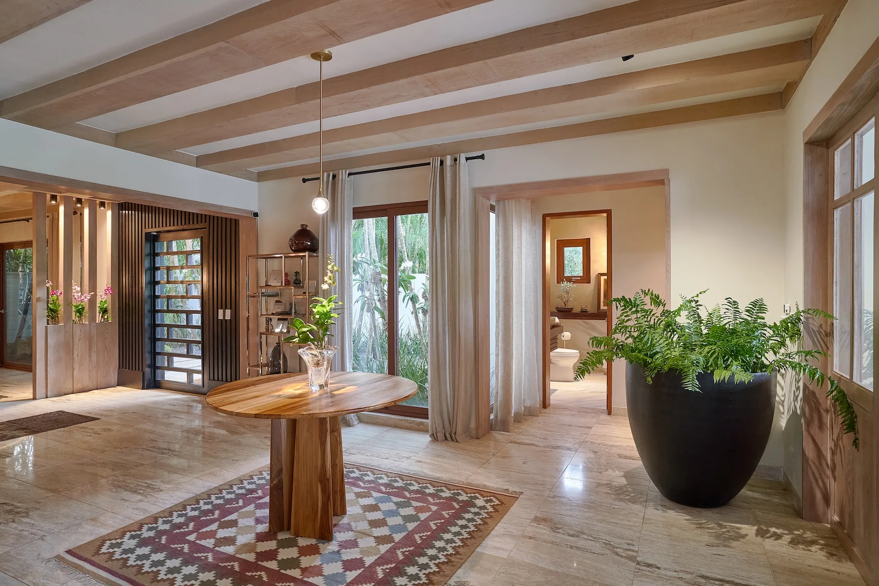 A bright interior room with exposed ceiling beams, a round table, and potted plants.