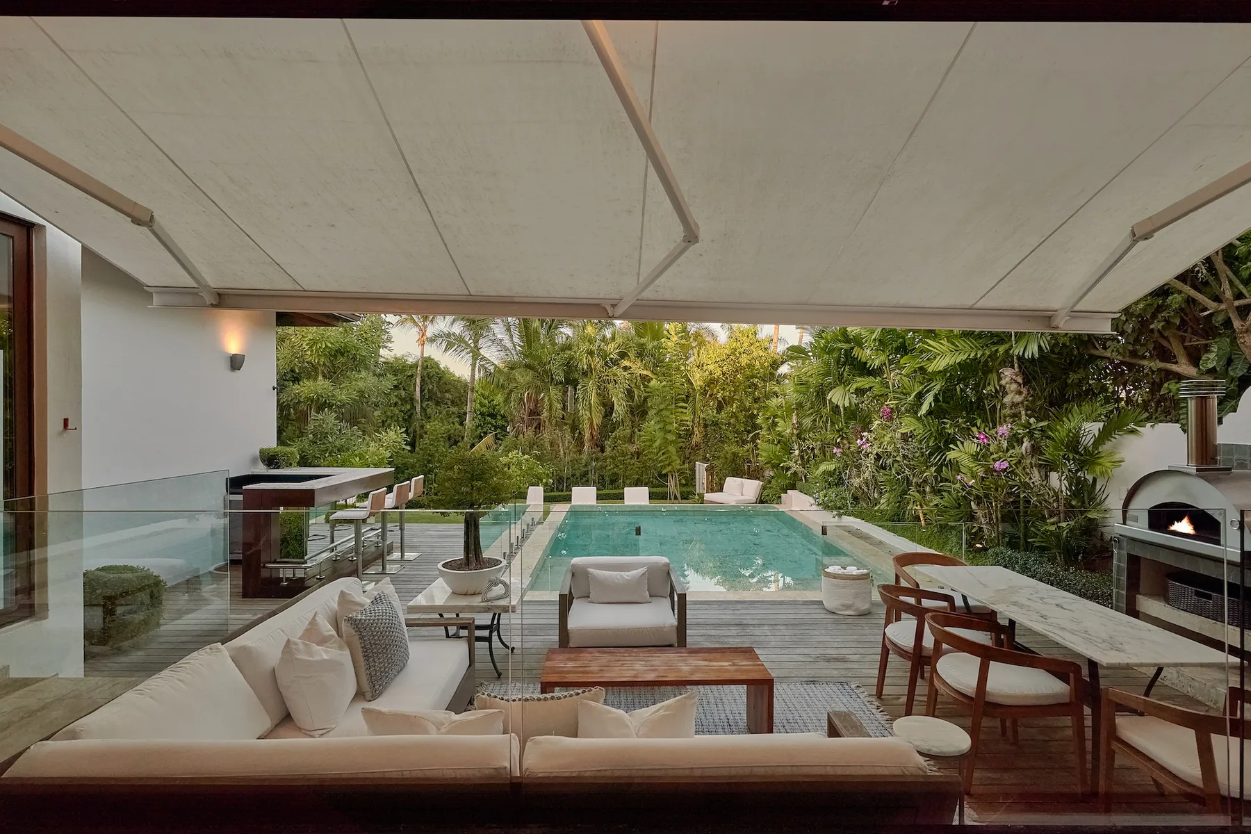 A covered outdoor seating area overlooks a swimming pool and lush greenery.