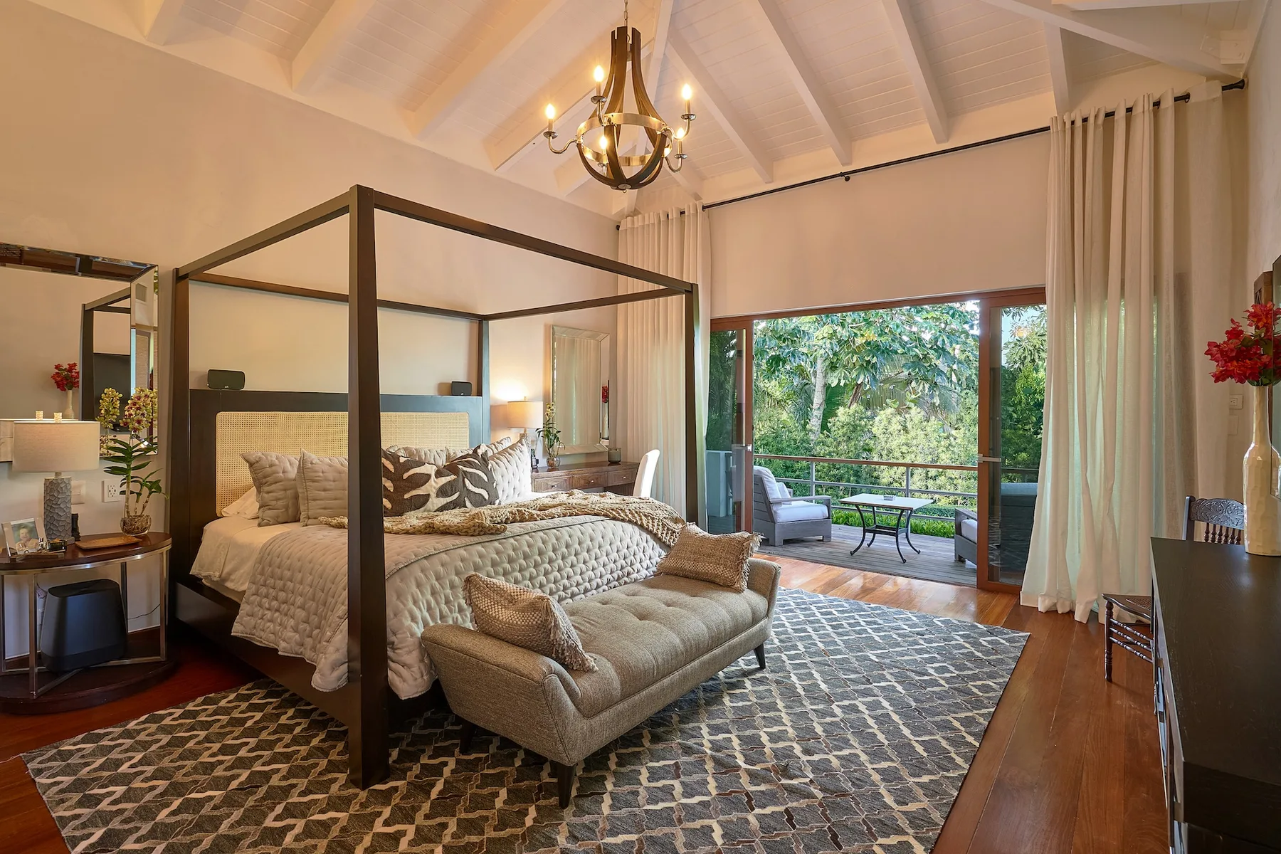 A bedroom with a canopy bed, seating area, and open doors to a garden patio.