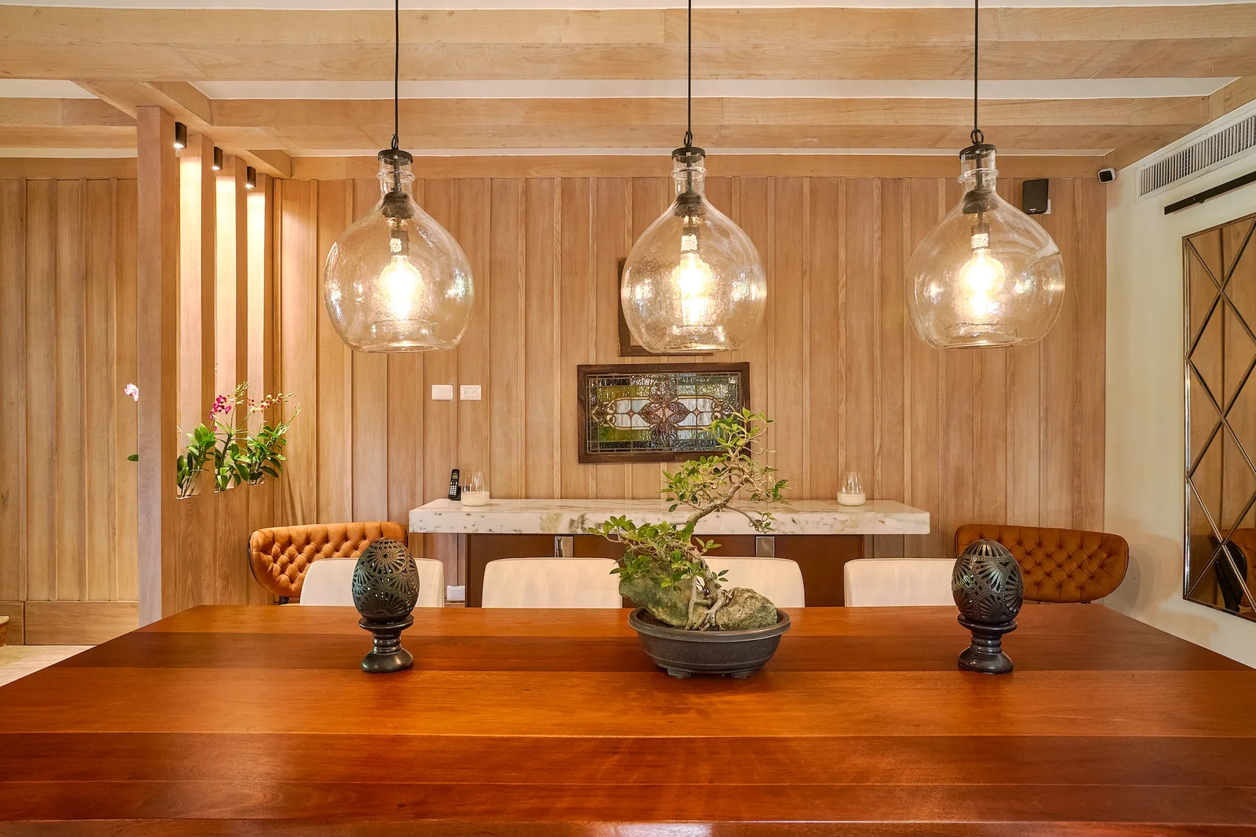 A warm wood-paneled dining area features a long table beneath three pendant lights.