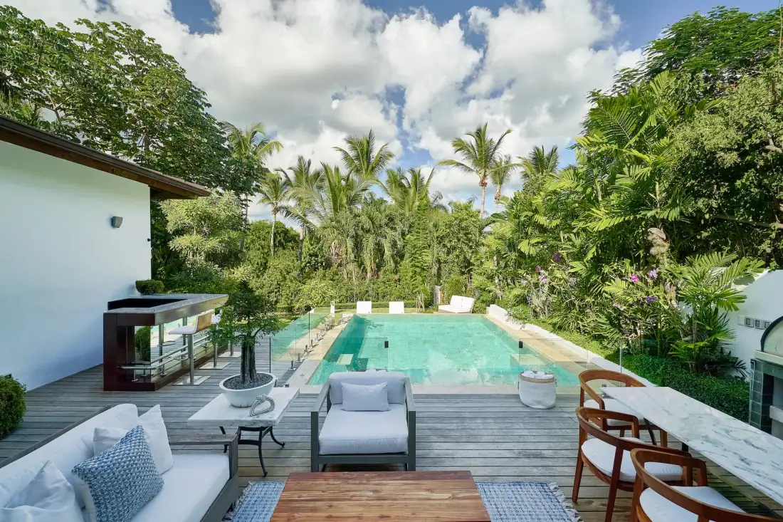 A swimming pool beside a wooden deck, surrounded by tropical greenery.