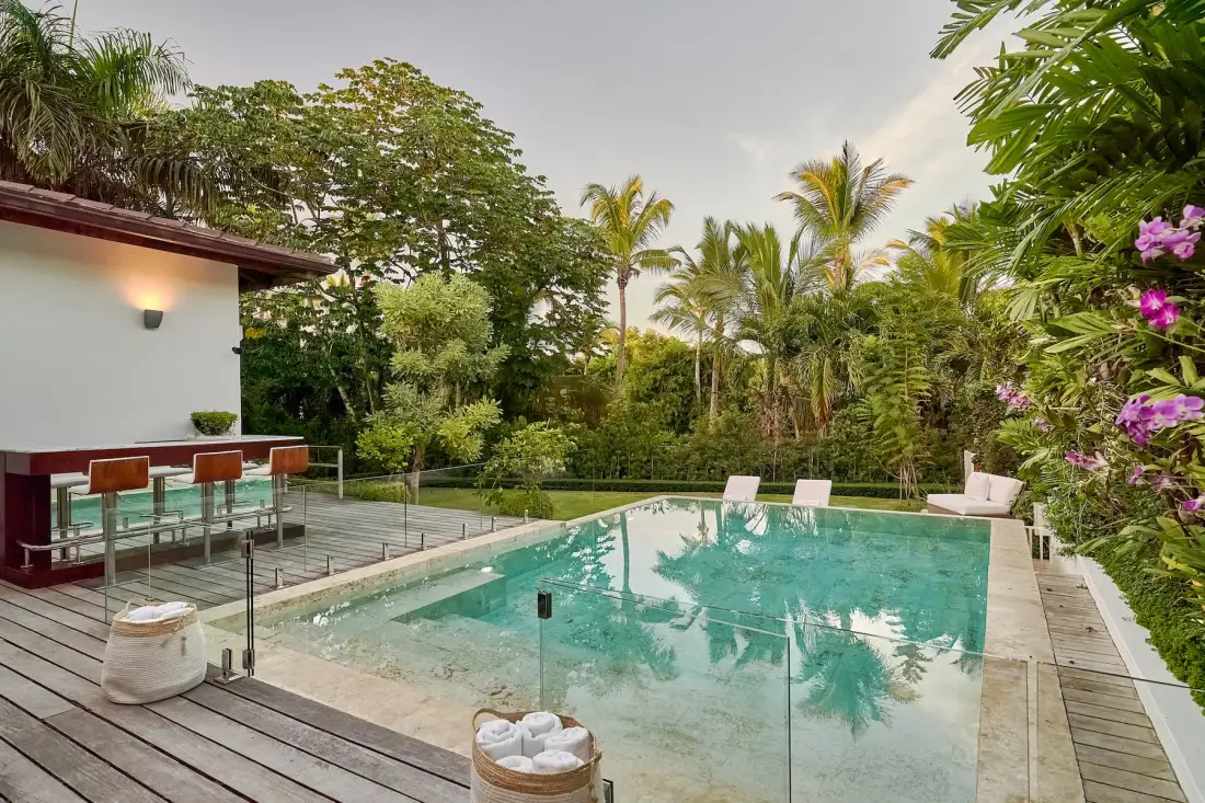 An outdoor swimming pool surrounded by tropical greenery and a wooden deck.