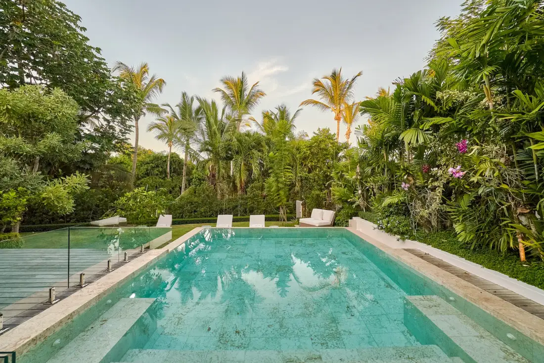 A rectangular swimming pool is surrounded by dense tropical greenery.