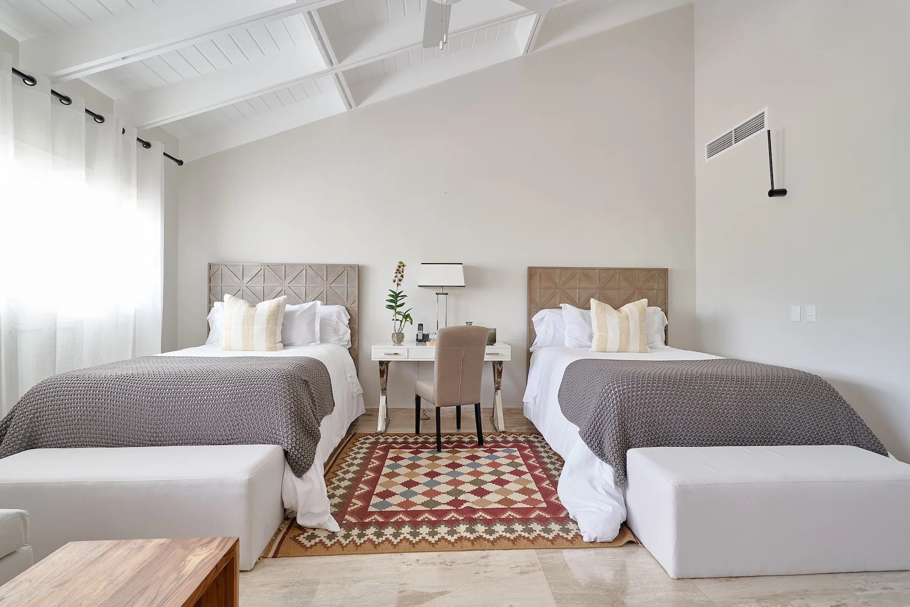 A bright bedroom has two beds with a small table between them.