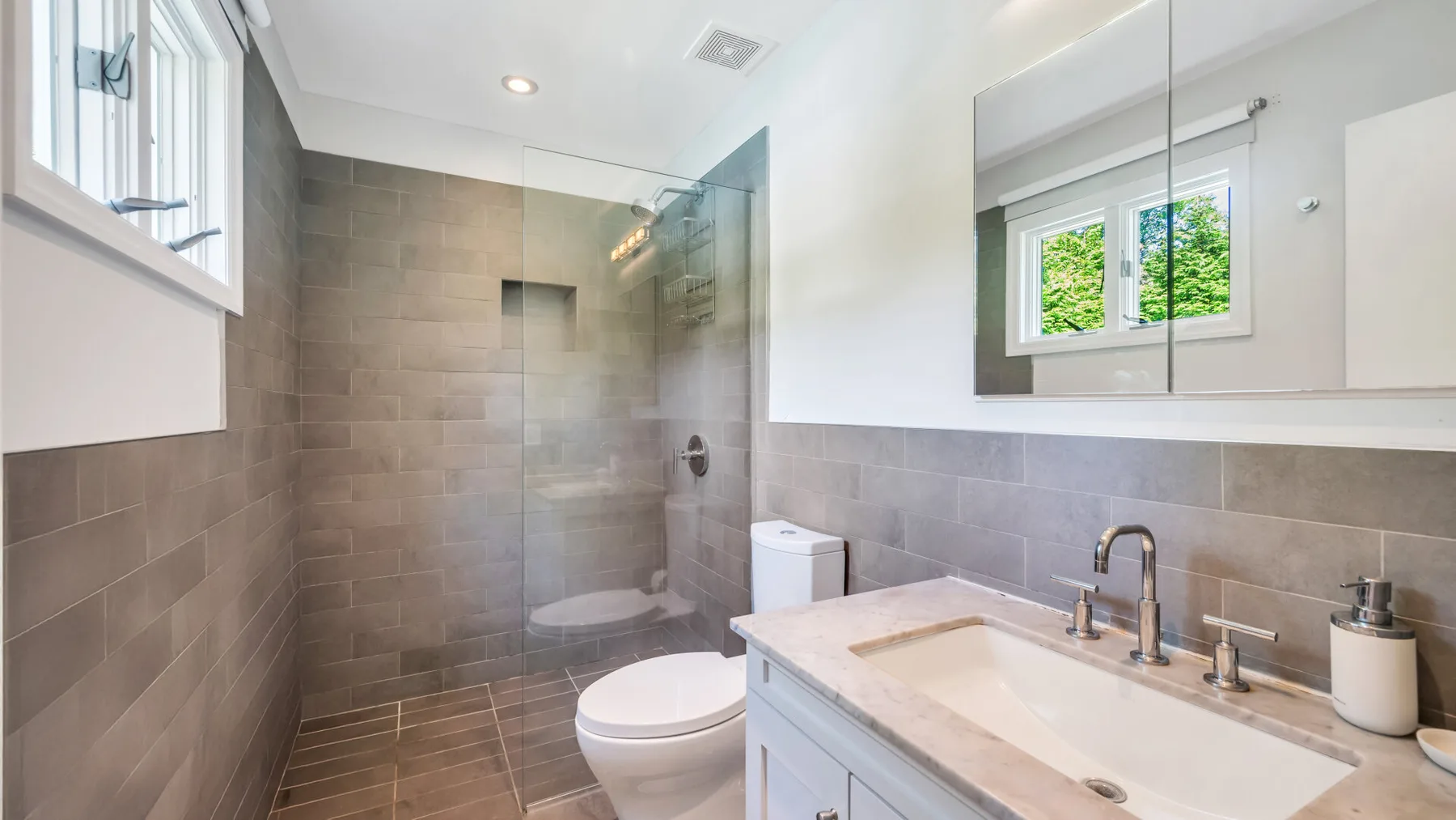 A bright bathroom with a glass shower, toilet, and sink.