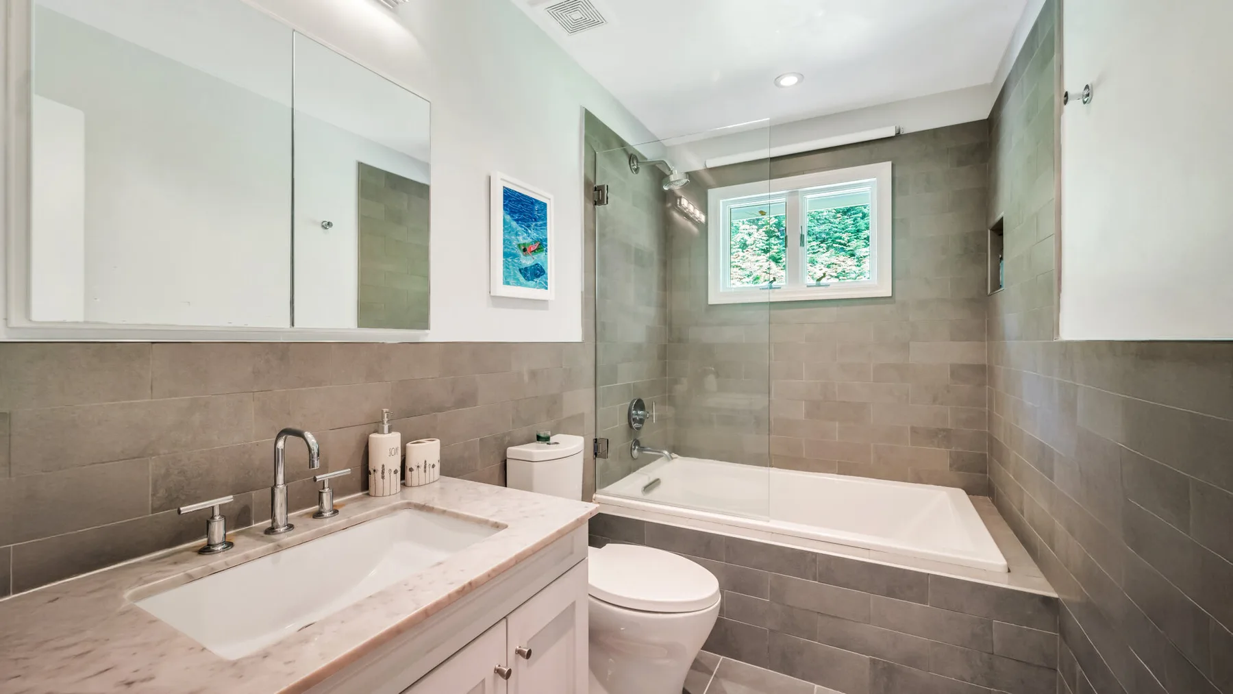 A bright bathroom with a bathtub, toilet, and sink beneath a window.