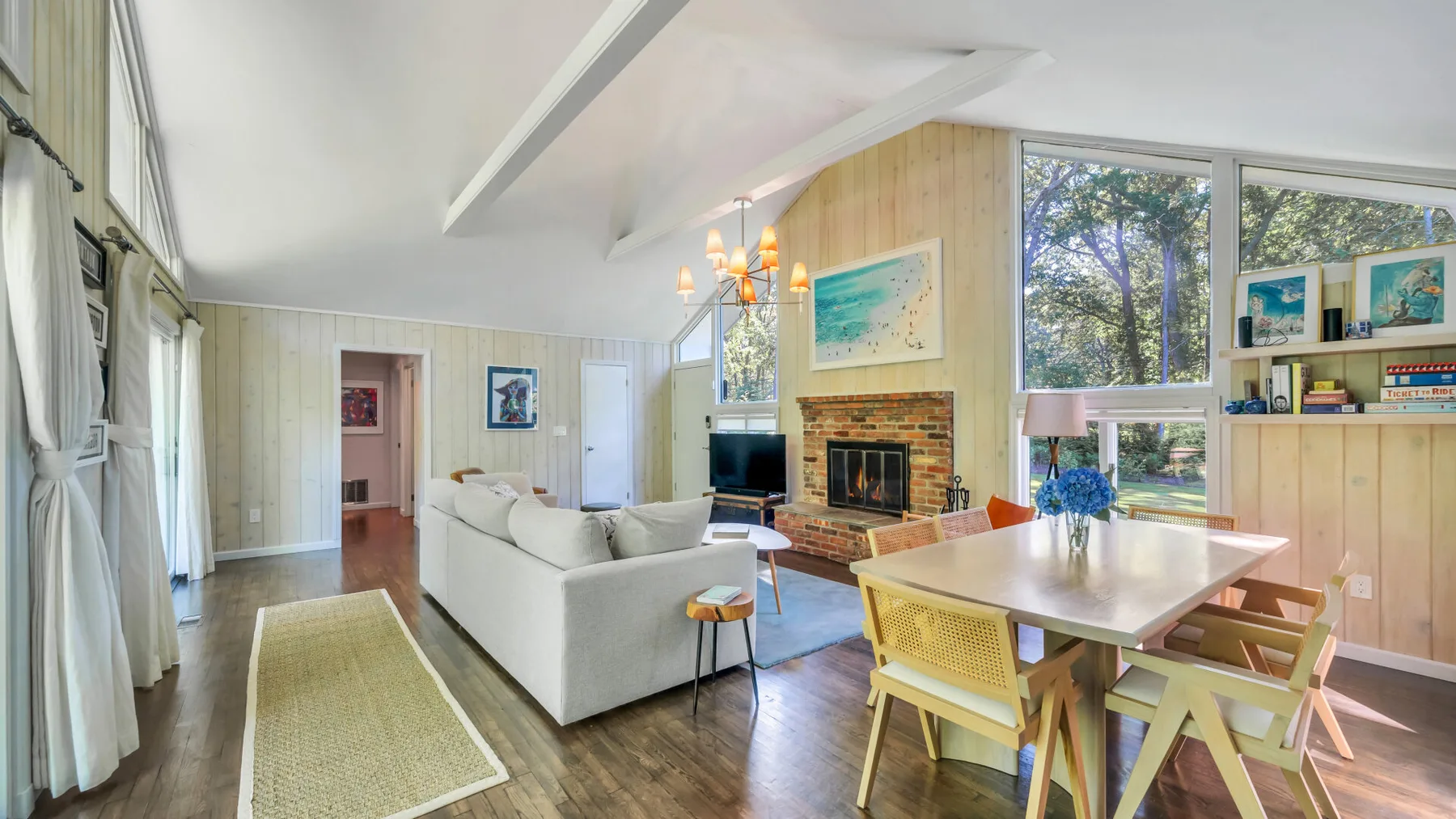 A bright living and dining room with large windows and a fireplace.