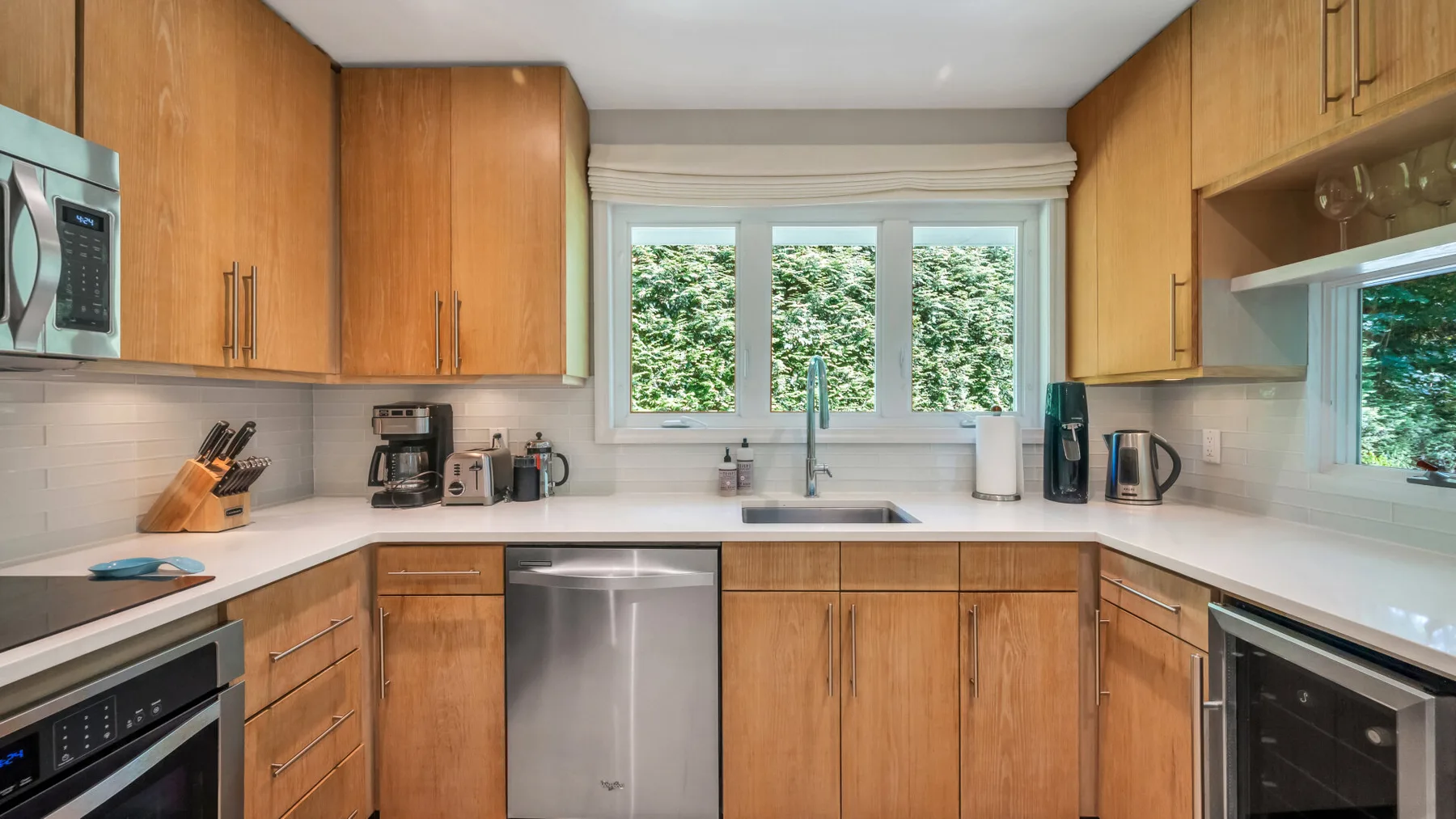 A kitchen with wooden cabinets, countertop appliances, and a window overlooking greenery.