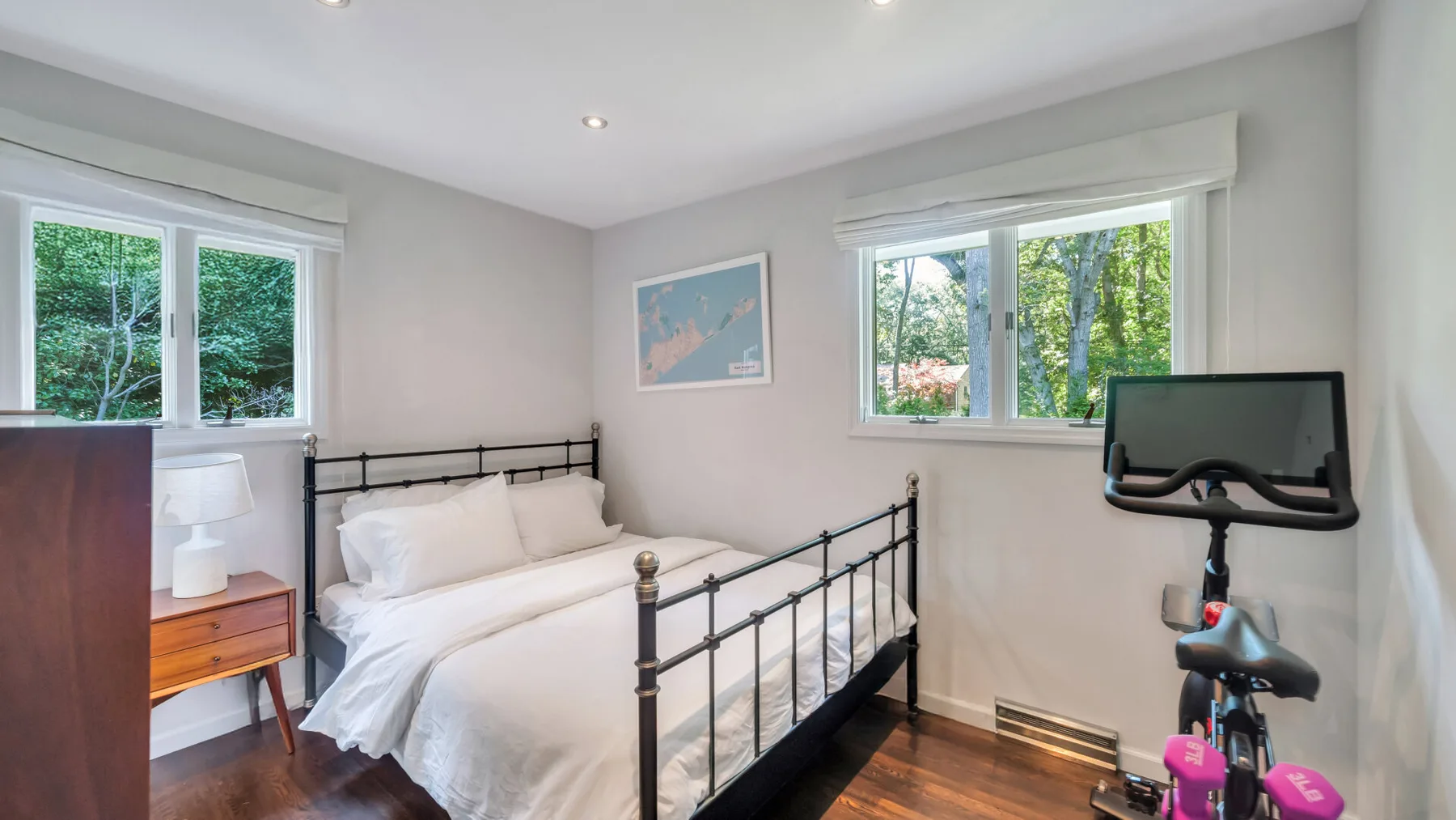 A bright bedroom with a metal bed and windows overlooking greenery.